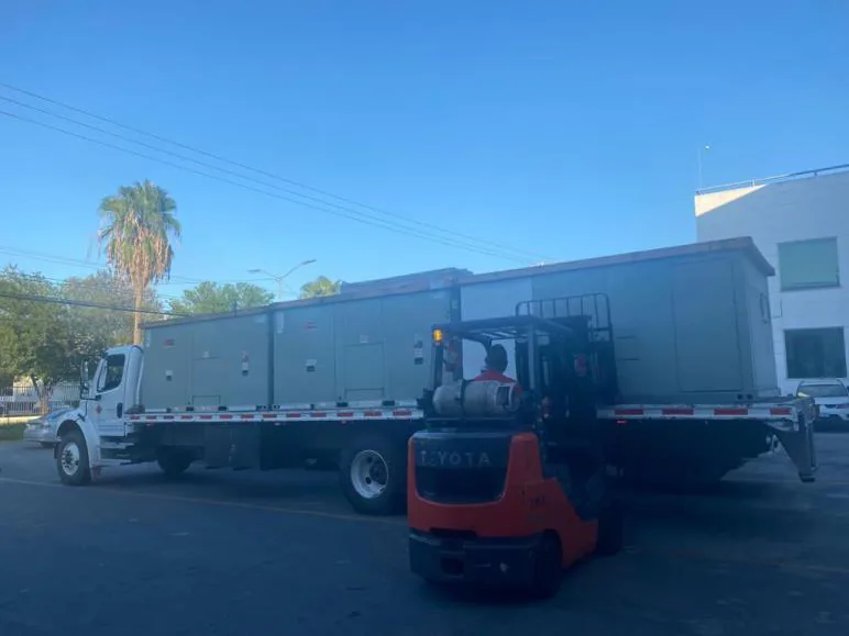 Unidades HVAC tipo paquete sobre camión plataforma en exterior, con montacargas maniobrando para la descarga