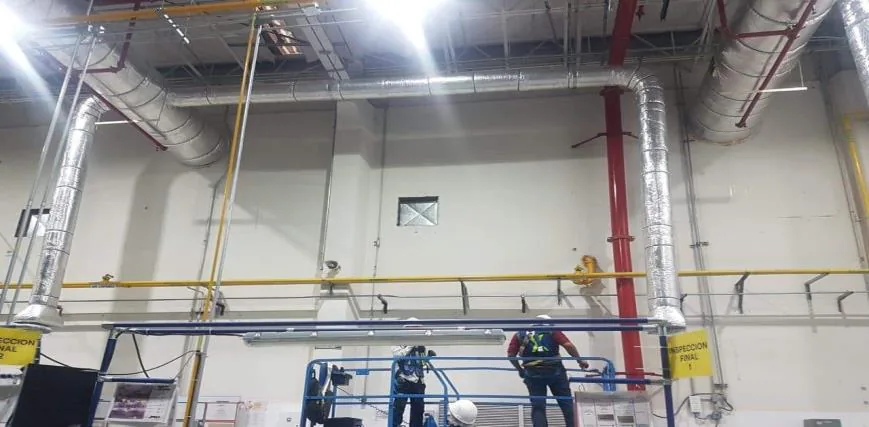 Dos trabajadores instalando espiroducto con aislamiento térmico plateado y codos de bajada sobre muro