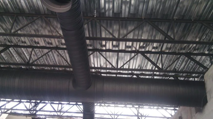 Ducto flexible oscuro colgado bajo techo de lámina con estructura metálica